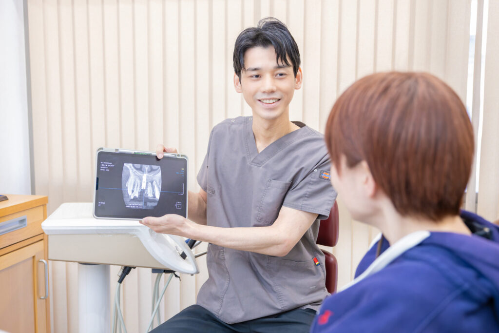 Clinician in gray scrubs shows a tablet with a dental X-ray to a patient in a clinic.